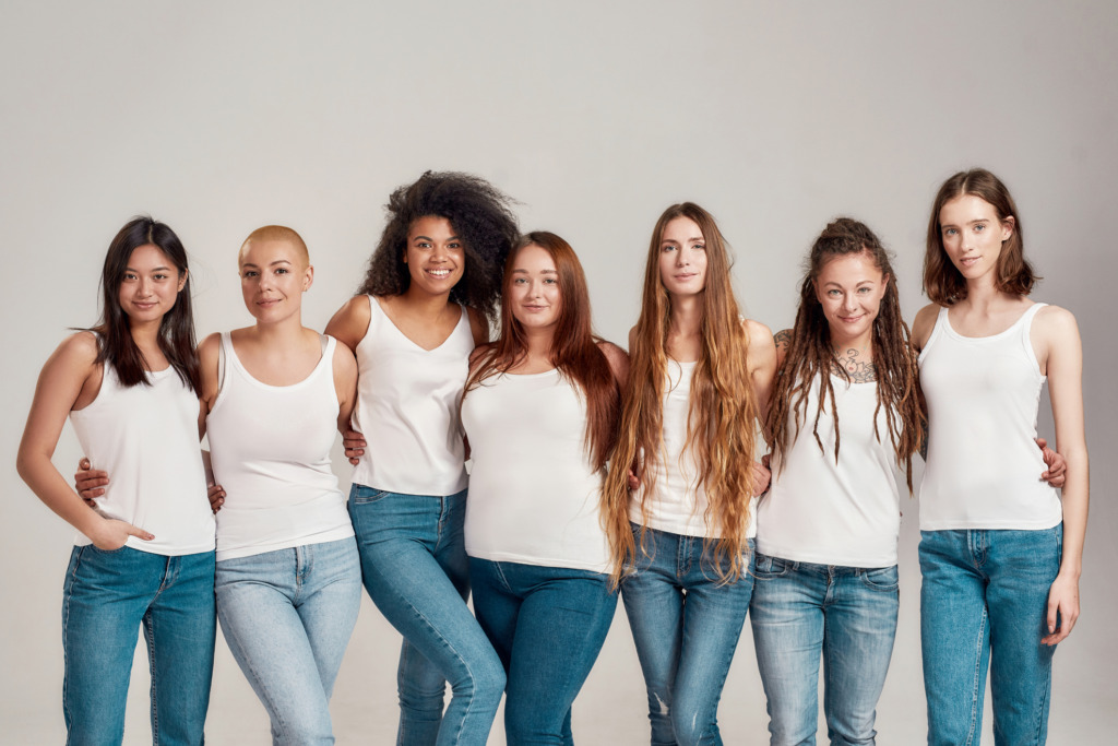 Group of young women wearing white shirt and denim jeans looking at camera while posing together